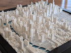 The Chicago 3D Map is a detailed white cityscape model with buildings of different heights, dense urban layout, roads, and small sections for parks or water, resembling a realistic 3D map.