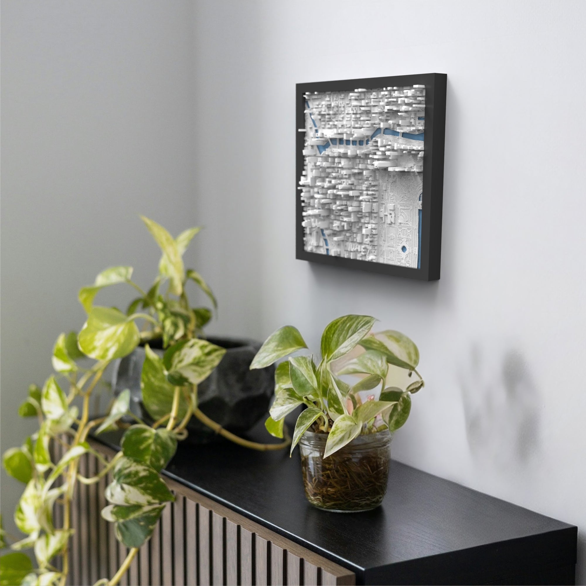 The Chicago 3D Map, a framed abstract wall art with a textured surface, hangs above a black shelf of leafy potted plants, evoking the dynamic contours of Chicago’s skyline.