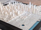 Chicago 3D Map: A detailed white 3D-printed cityscape inspired by the Chicago Skyline, featuring numerous buildings and a park with paths, trees, and a pond, all set on a black base.
