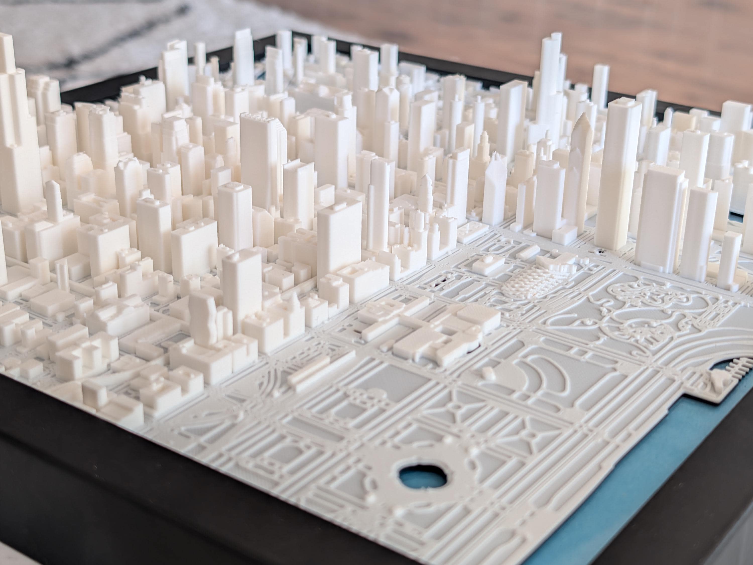 Chicago 3D Map: A detailed white 3D-printed cityscape inspired by the Chicago Skyline, featuring numerous buildings and a park with paths, trees, and a pond, all set on a black base.