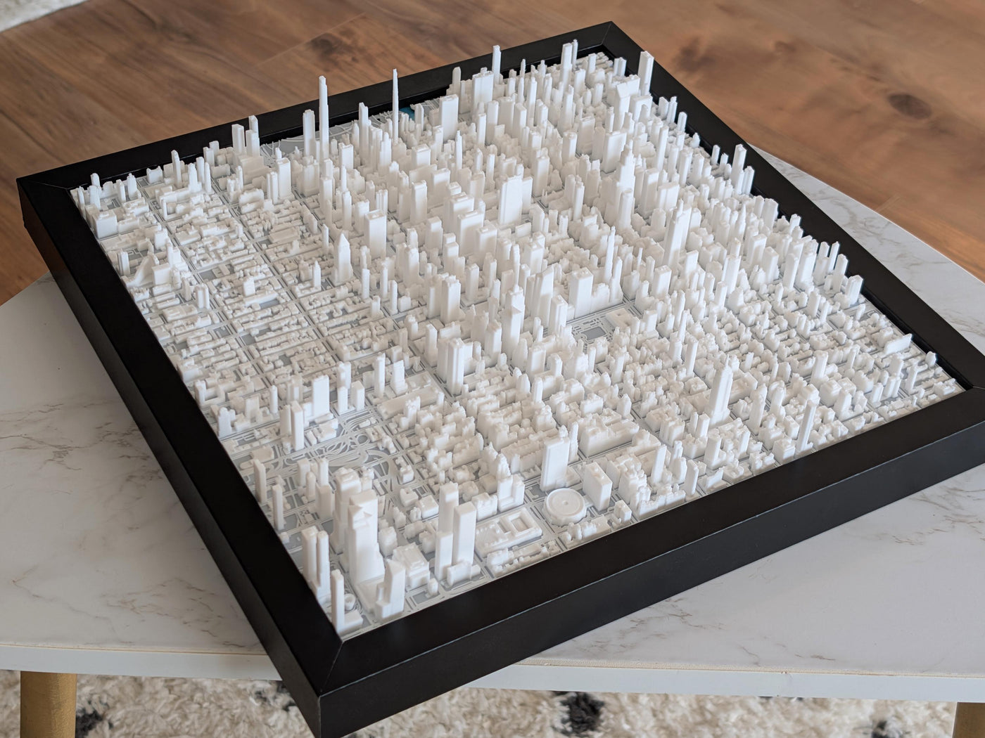 A framed 3D printed map of NYC's Midtown Manhattan, featuring white buildings and streets on a black background.